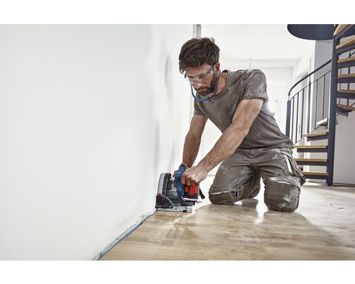 Bărbat taie podea de lemn cu un ferăstrău vertical.