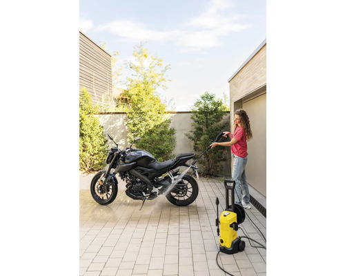 Femeie curăță motocicletă cu un curățător cu presiune înaltă pe o suprafață pavată