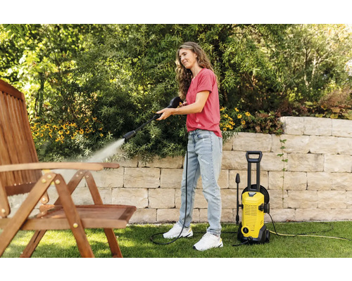 Femeie curățând un scaun de lemn cu un aparat de curățat cu presiune înaltă în grădină.