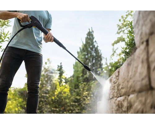 Persoană care curăță un zid de piatră cu un aparat de curățat cu presiune