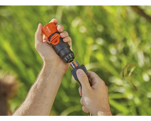 O persoană conectează un conector Gardena cu opritor de apă la un furtun de grădină.