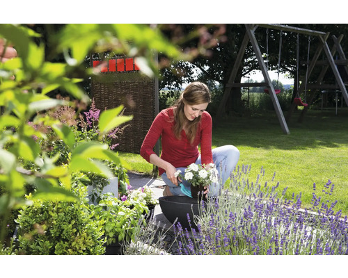 O femeie plantează o floare într-un ghiveci în grădină.