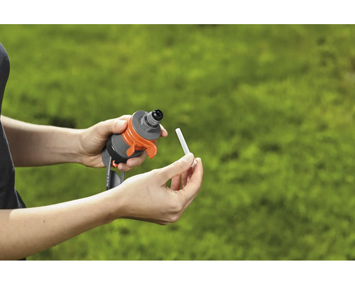 Mâinile introduc un baton de fertilizare într-un dispozitiv de irigare pentru grădină