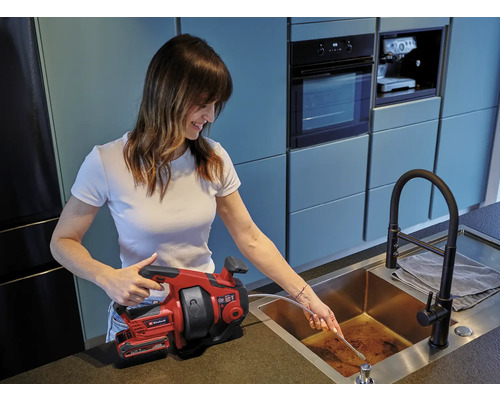 Femeie care folosește un șarpe de instalații sanitare Einhell pentru a desface o conductă de scurgere.