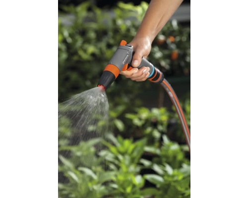 O mână ține un pulverizator de grădină care stropește cu apă.