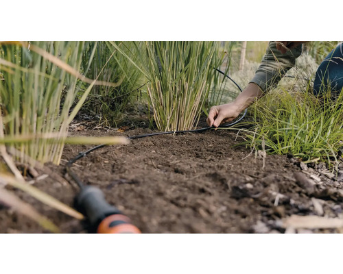 O persoană instalează un sistem de irigații în grădină.