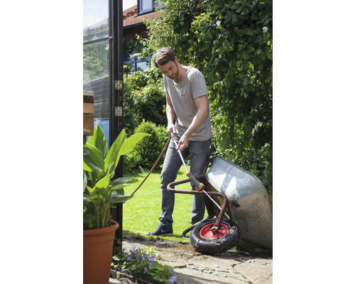 Un bărbat curăță o roabă cu un furtun de grădină în grădină.