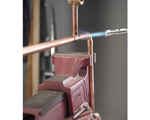 Conductă de cupru conectată cu un pistol de lipit și un banc de lucru