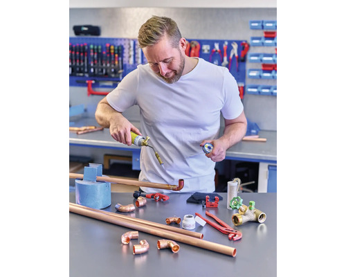 Un bărbat sudează țevi de cupru cu un arzător cu gaz într-un atelier.