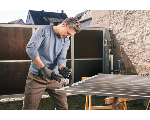 Bărbat șlefuind o poartă metalică cu un polizor unghiular în aer liber.