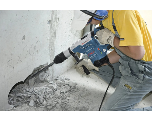 Un muncitor folosește un ciocan rotopercutor pentru a da o gaură într-un perete de beton.