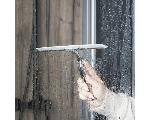 O persoană folosește o racletă de duș pentru a curăța un perete de duș.