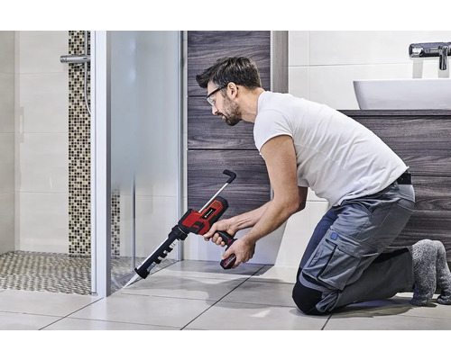 Un meșter folosește un pistol de etanșare fără fir în baie pentru a etanșa o cabină de duș.