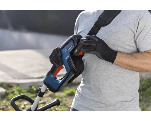 O persoană schimbă bateria unui trimmer de gazon cu acumulator Bosch cu curea de transport