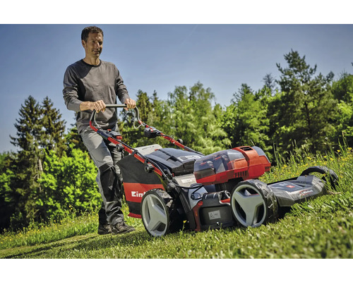Un bărbat împinge o mașină de tuns iarba cu acumulator Einhell pe un gazon.