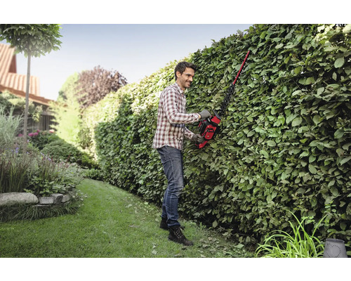 Un bărbat tunde un gard viu într-o grădină folosind un tăietor de gard viu.