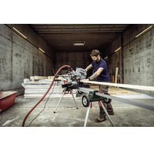 Un bărbat taie o scândură de lemn cu un fierăstrău circular Metabo pe o masă de tăiat.