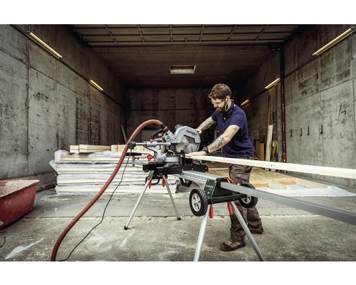 Un bărbat taie o scândură de lemn cu un fierăstrău circular Metabo pe o masă de tăiat.