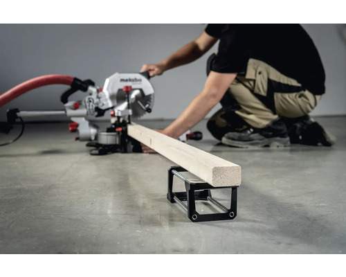 Un ferăstrău circular Metabo taie o scândură de lemn care se află pe un suport pentru piese de prelucrat.