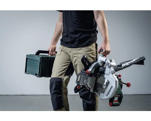 O persoană care transportă un ferăstrău circular de retezare Metabo și o cutie de scule.