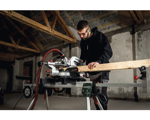 Un bărbat taie lemn cu un ferăstrău circular Metabo pe un suport pentru ferăstrău circular într-o clădire în construcție.