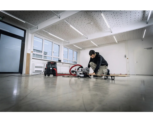 O persoană lucrează cu un ferăstrău circular și un aspirator într-o cameră luminoasă.