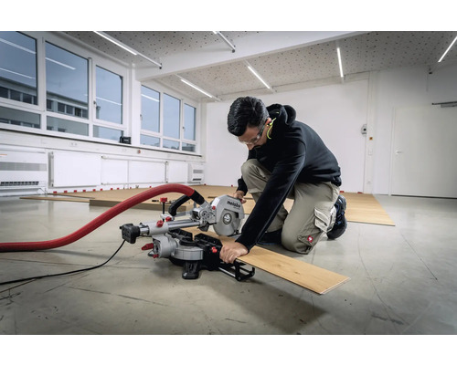 O persoană taie o scândură de lemn cu un ferăstrău circular Metabo într-o cameră cu podea din lemn.