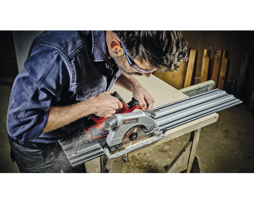 Un bărbat taie o scândură de lemn cu un ferăstrău vertical și o șină de ghidare de la Einhell.