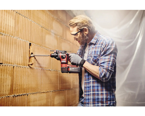 Un bărbat găurește un perete de cărămidă cu un ciocan rotopercutor.