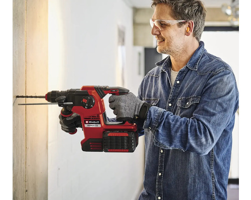 Un bărbat găurește un perete cu un ciocan rotopercutor cu acumulator Einhell Herocco.