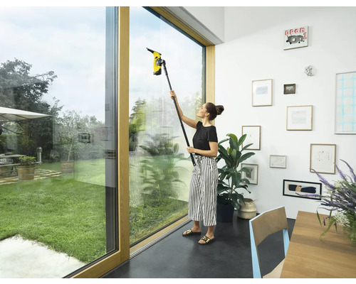 Femeie curăță ferestrele cu un aspirator de geamuri în interior.