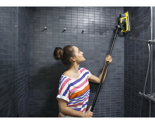 Femeie curăță un duș cu gresie cu o racletă cu mâner telescopic