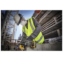 Un muncitor în construcții folosește un polizor unghiular pe un șantier și poartă echipament de protecție.