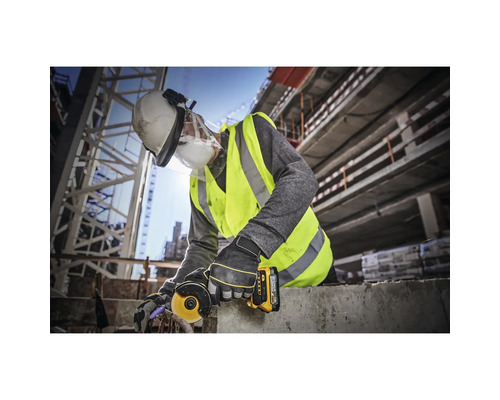 Un muncitor în construcții folosește un polizor unghiular pe un șantier și poartă echipament de protecție.