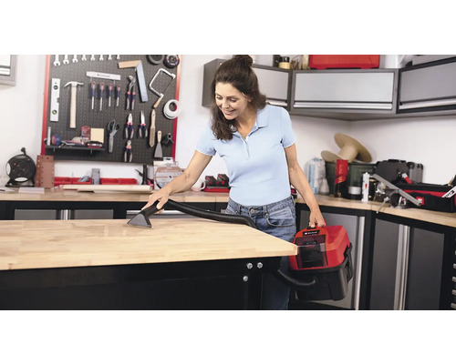 O femeie curăță un banc de lucru cu un aspirator umed și uscat într-un atelier.