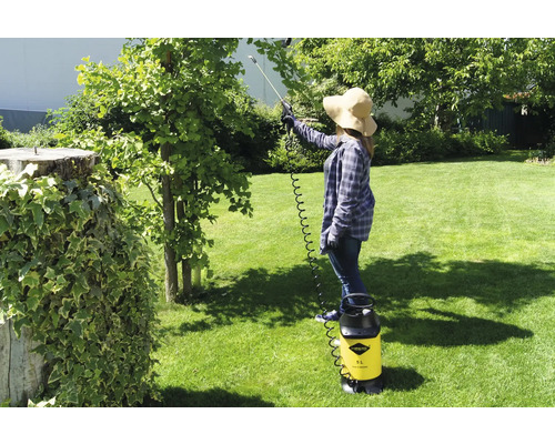 Femeie folosind un pulverizator cu presiune galben de la Mesto în grădină pentru a trata un copac.