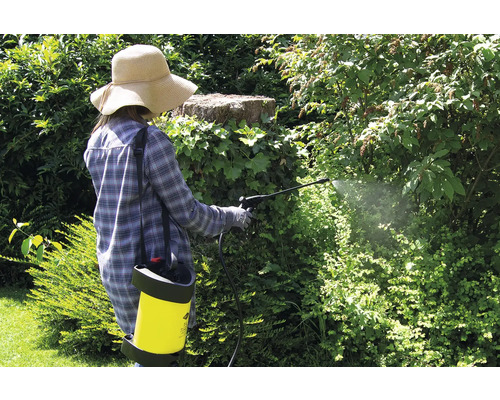 Femeie în grădină pulverizând plante cu pesticide și pulverizator de spate