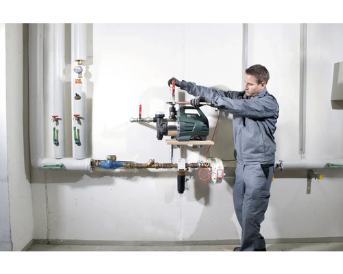 Instalarea unei pompe de grădină de către un meseriaș pe un perete cu țevi.