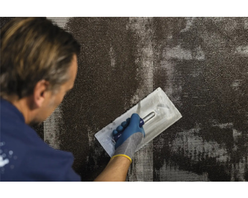 Un bărbat aplică mortar de armare pe o țesătură cu ajutorul unei mistrii de tencuială.