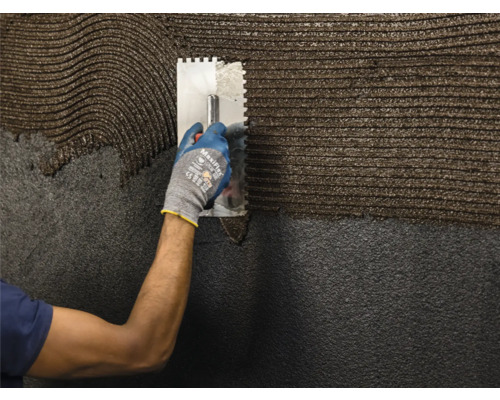 O persoană aplică adeziv cu o spatulă pe o suprafață