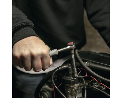 O persoană folosește o cheie cu clichet cu o priză pe un motor.