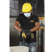 Un meșter forează cu o mașină de găurit cu acumulator într-un bloc de beton, în timp ce poartă îmbrăcăminte de protecție.