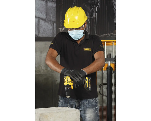 Un meșter forează cu o mașină de găurit cu acumulator într-un bloc de beton, în timp ce poartă îmbrăcăminte de protecție.