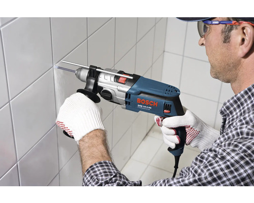 Un bărbat găurește un perete cu faianță cu o mașină de găurit cu percuție Bosch.