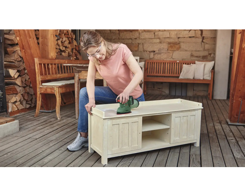 Femeie șlefuind un dulap din lemn cu un șlefuitor excentric în aer liber.