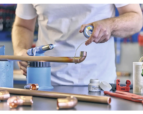 Artizan care sudează o țeavă de cupru cu o lampă de lipit și cositor de lipit