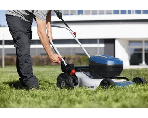 O persoană folosește o mașină de tuns iarba cu acumulator pe un gazon în fața unei case.