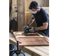 Bărbat șlefuind o ușă de lemn cu șlefuitor oscilant într-un atelier