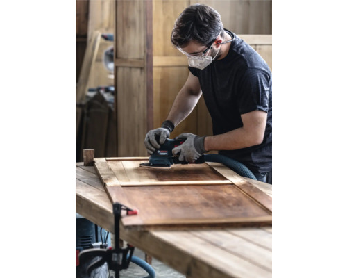 Bărbat șlefuind o ușă de lemn cu șlefuitor oscilant într-un atelier