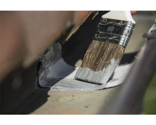 Vopsirea unei jgheaburi cu o pensulă.